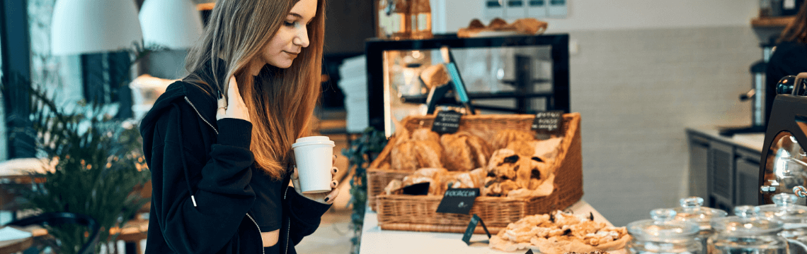 Woman buying pastry at shop woman holding coffee looking at pastries on counter