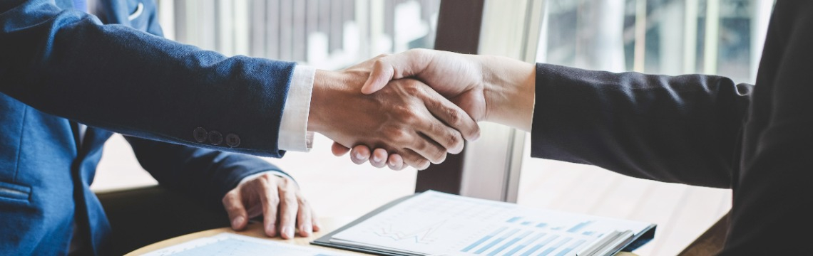 Handshake business agreement Hands shaking over a desk with paperwork