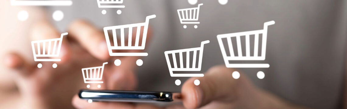 Virtual shopping carts emerging from mobile phone held by hand.
