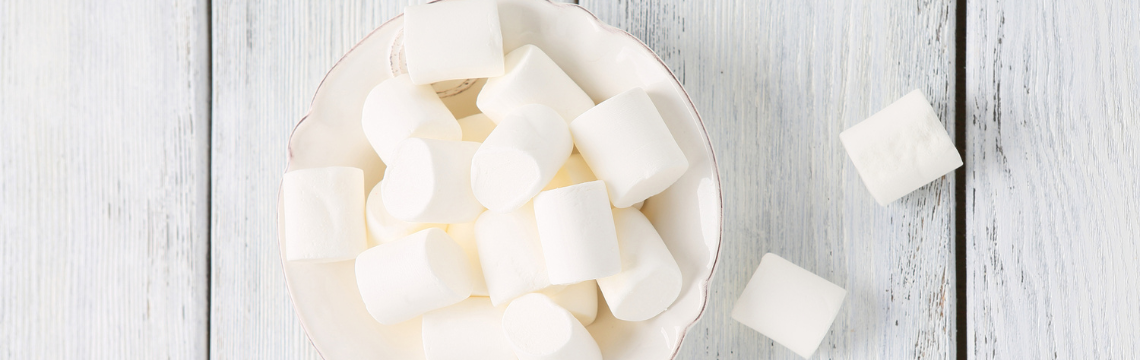 White bowl full of large marshmallows on a white-washed wood table.
