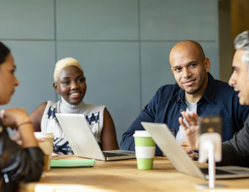 Team members having a discussion around a table with laptops
